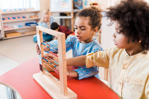 Selective focus of african american kids playing with scores with teacher and child at background in montessori school