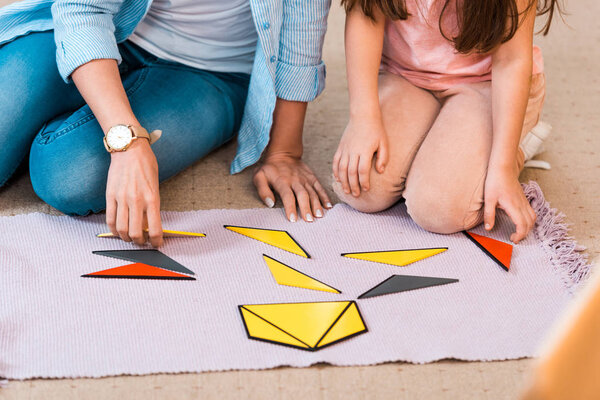 Cropped view of kid and teacher playing educational game on floor in montessori class