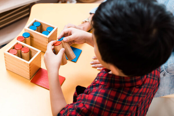 Selective focus of kid and teacher playing wooden game at desk in montessori school, overhead view