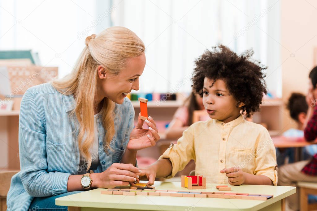 African american child playing educational game with smiling teacher in montessori school