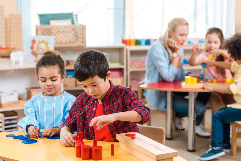 Selective focus of kids playing games with children and teacher at background in montessori school 