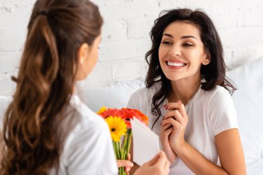 Anneler gününde elinde bir buket gerbera tutan kızına bakan mutlu bir kadın.