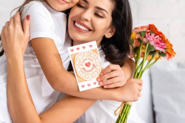 Mutlu kadın, elinde çiçeklerle kızına sarılıyor ve anneler günü kartı atıyor. Seni seviyorum anne yazıtları.