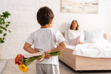 Anne yatakta otururken çocuğun elinde çiçekler ve anneler günü kartı vardı. 