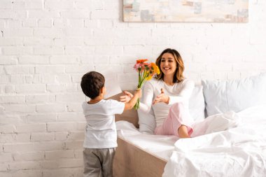 Mutlu anneye çiçek ve anneler günü kartı sunan çocuğun arka planı.