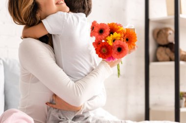 Anneler Günü 'nde elinde çiçeklerle oğlunu kucaklayan mutlu anne manzarası.