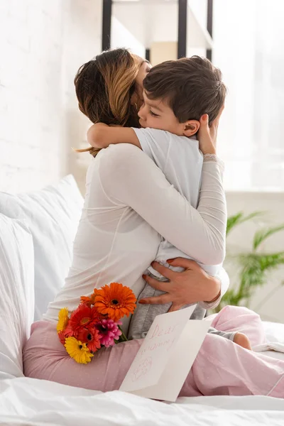 Feliz Madre Abrazando Adorable Hijo Mientras Está Sentado Cama Cerca — Foto de Stock