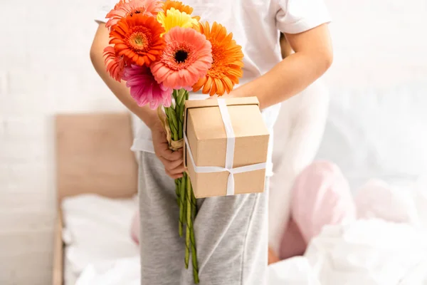 ベッドに座っている母親の近くで花や母の日の贈り物を持っている男の子の背中のビュー — ストック写真