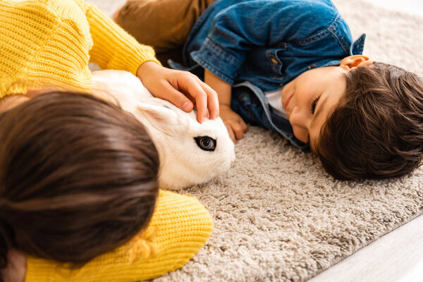 милый брат и сестра лежат на полу возле белого смешного кролика
