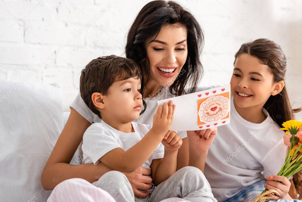 happy woman reading mothers day card while sitting in bed with adorable children