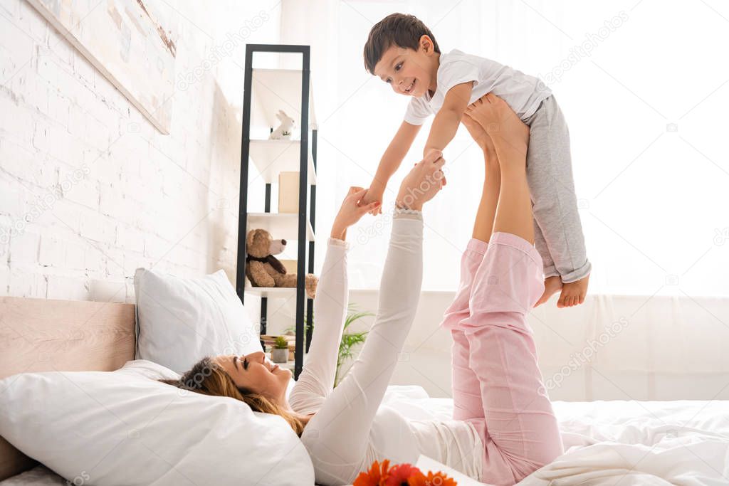 happy woman having fun with adorable son in bed on mothers day