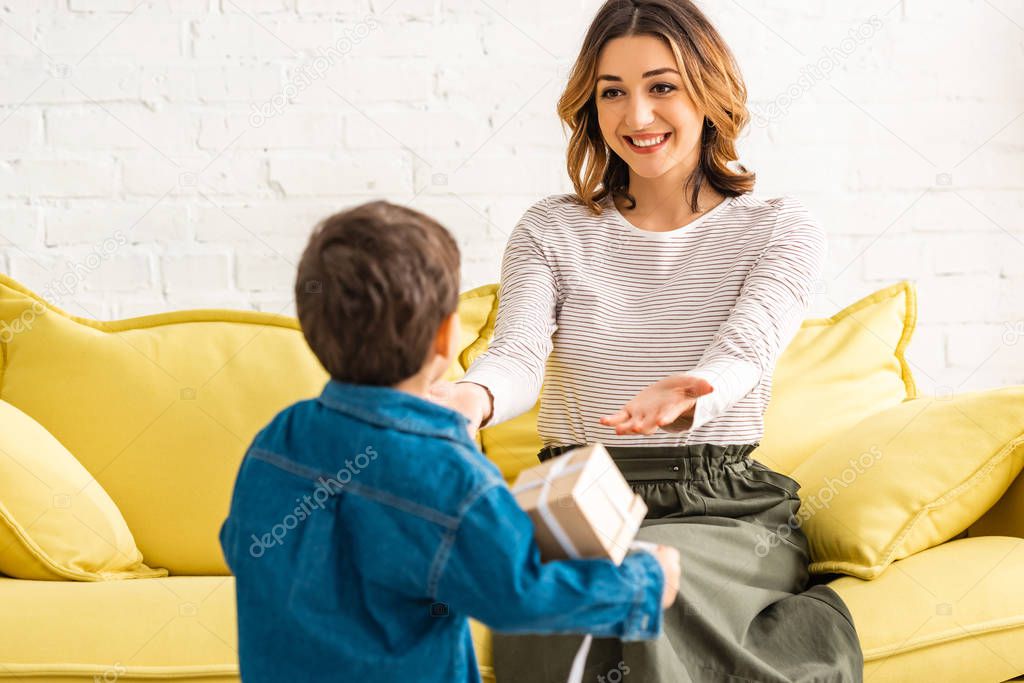 happy woman outstretching hands to adorable son holding gift box on mothers day