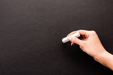 cropped view of woman holding chalk near on empty black chalkboard clipart