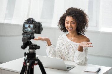 Seçici odak, dijital kameranın yanında el kol hareketi yapan neşeli Afrikalı Amerikalı video blogcusu. 