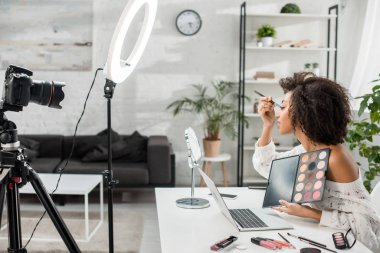 Afro-Amerikan video blogcusu göz farı uyguluyor ve dijital kameraya bakıyor. 