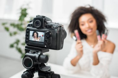 Ekranda dudak parlatıcısı tutan kıvırcık Afrikalı Amerikalı video blogcusu olan dijital kameranın seçici odağı 