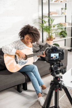 Dijital kameranın yanında akustik gitar çalan genç ve kıvırcık Afrikalı Amerikalı kızın seçici odağı 
