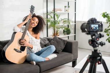 Akustik gitar tutan ve dijital kameraya bakan mutlu Afrikalı Amerikalı kızın seçici odak noktası 