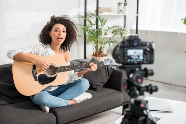 Akustik gitar çalan ve dijital kameranın yanında şarkı söyleyen Afrikalı Amerikalı genç bir kızın seçici odak noktası. 