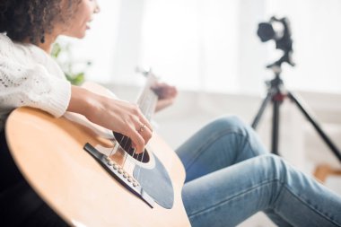 Dijital kameranın yanında akustik gitar çalan Afrikalı Amerikalı genç bir kız görüntüsü. 