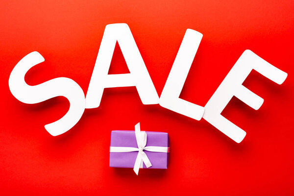 top view of white sale lettering near gift box on red background
