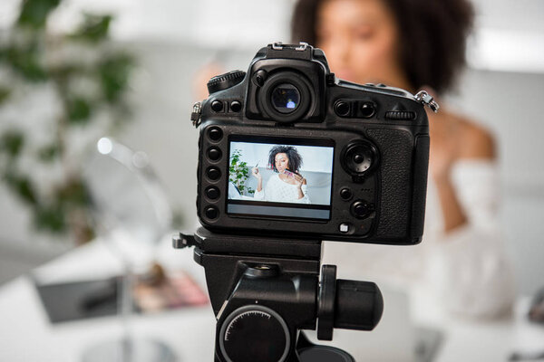 selective focus of digital camera with african american girl holding palette with lip gloss and cosmetic brush on display 