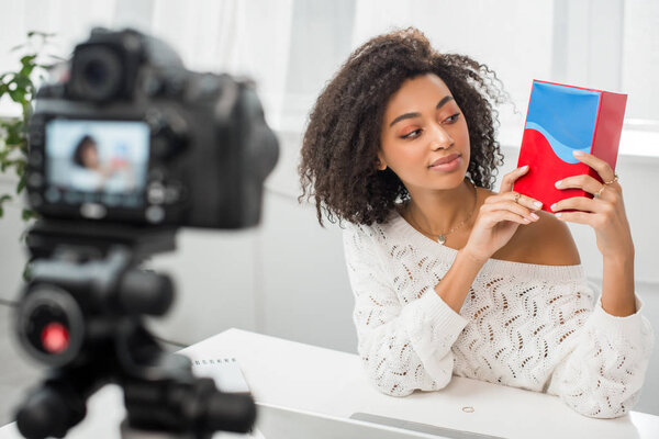 selective focus of happy african american influencer looking at colorful box near digital camera 