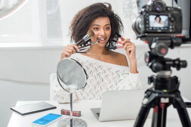 Kyiv, Ukrayna - 10 Aralık 2019: diş telli, dudak parlatıcısı ve akıllı telefonun yanında Skype uygulamalı kozmetik fırçalar tutan Afrikalı Amerikalı bir kızın seçici odak noktası 