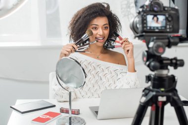 Kyiv, Ukrayna - 10 Aralık 2019: diş telli, dudak parlatıcısı ve akıllı telefonun yanında Youtube uygulamalı kozmetik fırça tutan Afro-Amerikan kadının seçici odak noktası 