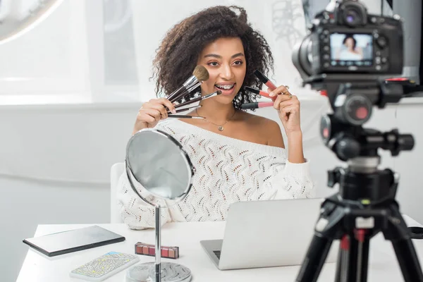 快乐的非洲裔美国影响者在智能手机附近拿着唇彩和化妆品刷 屏幕上的在线地图和数码相机的选择焦点 — 图库照片
