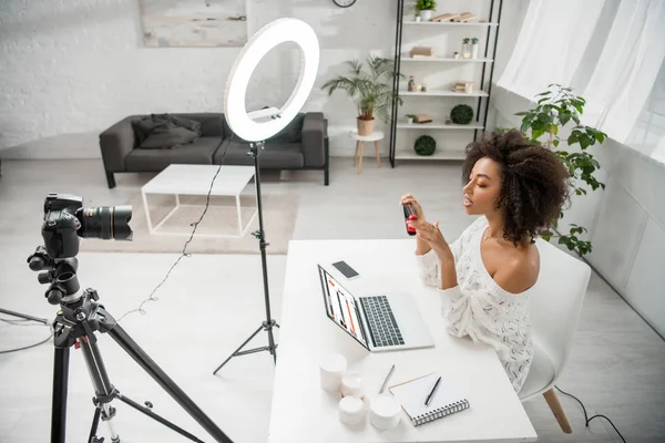 stock image KYIV, UKRAINE - DECEMBER 10, 2019: african american influencer holding hair straightener near digital camera and laptop with soundcloud website 