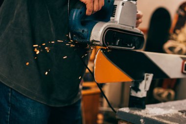 cropped view of worker repairing ski with belt sander in repair shop  clipart