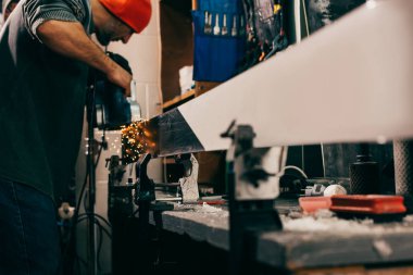 side view of worker repairing ski with belt sander in repair shop  clipart