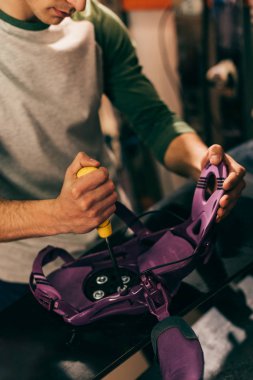 cropped view of worker screwing snowboard binding to snowboard in repair shop  clipart