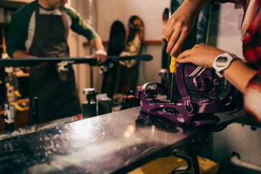 cropped view of worker screwing snowboard binding to snowboard in repair shop  clipart