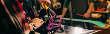 panoramic shot of worker screwing snowboard binding to snowboard in repair shop  clipart