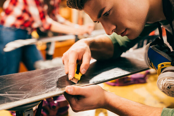 cropped view of worker using box cutter on ski in repair shop