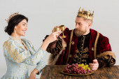usmívající se královna a král s korunami cinkání s poháry izolované na šedé