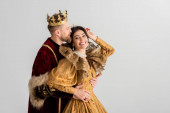 king with crown kissing and hugging smiling queen isolated on grey