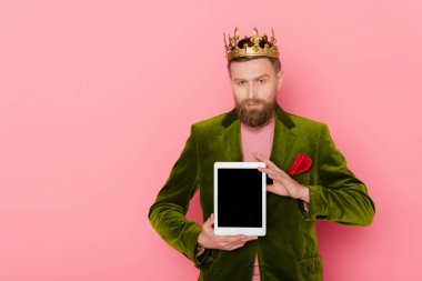 Kadife ceketli yakışıklı adam elinde pembe arka planda dijital tablet tutuyor. 