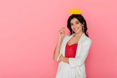 smiling woman holding paper crown looking at camera on pink background  clipart