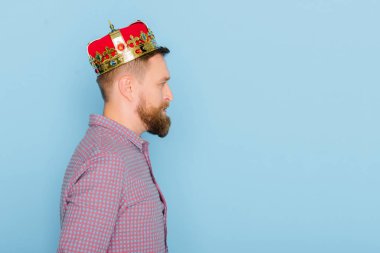 side view of handsome man with crown isolated on blue  clipart