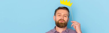 panoramic shot of man holding paper crown on blue background  clipart