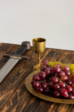 Antik fincan, kılıç ve üzüm Gri üzerinde izole ahşap masa üzerinde