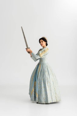 attractive queen with crown holding sword on grey background 