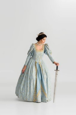 attractive queen with crown holding sword on grey background 
