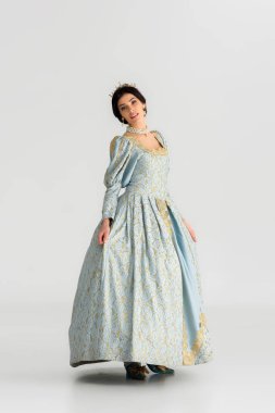 attractive queen in dress with crown looking at camera on grey background 