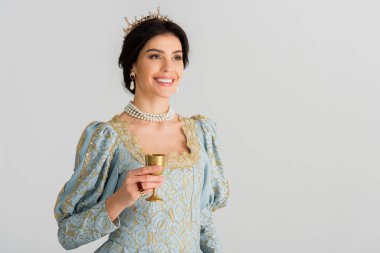 smiling queen with crown holding cup isolated on grey