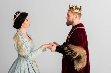 side view of queen and king with crowns holding hands isolated on grey 