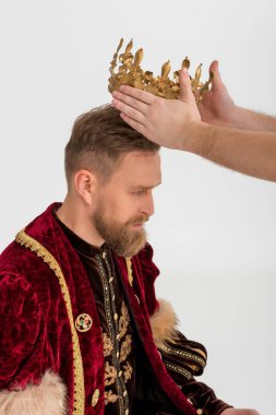 cropped view of man putting crown on king on grey background 